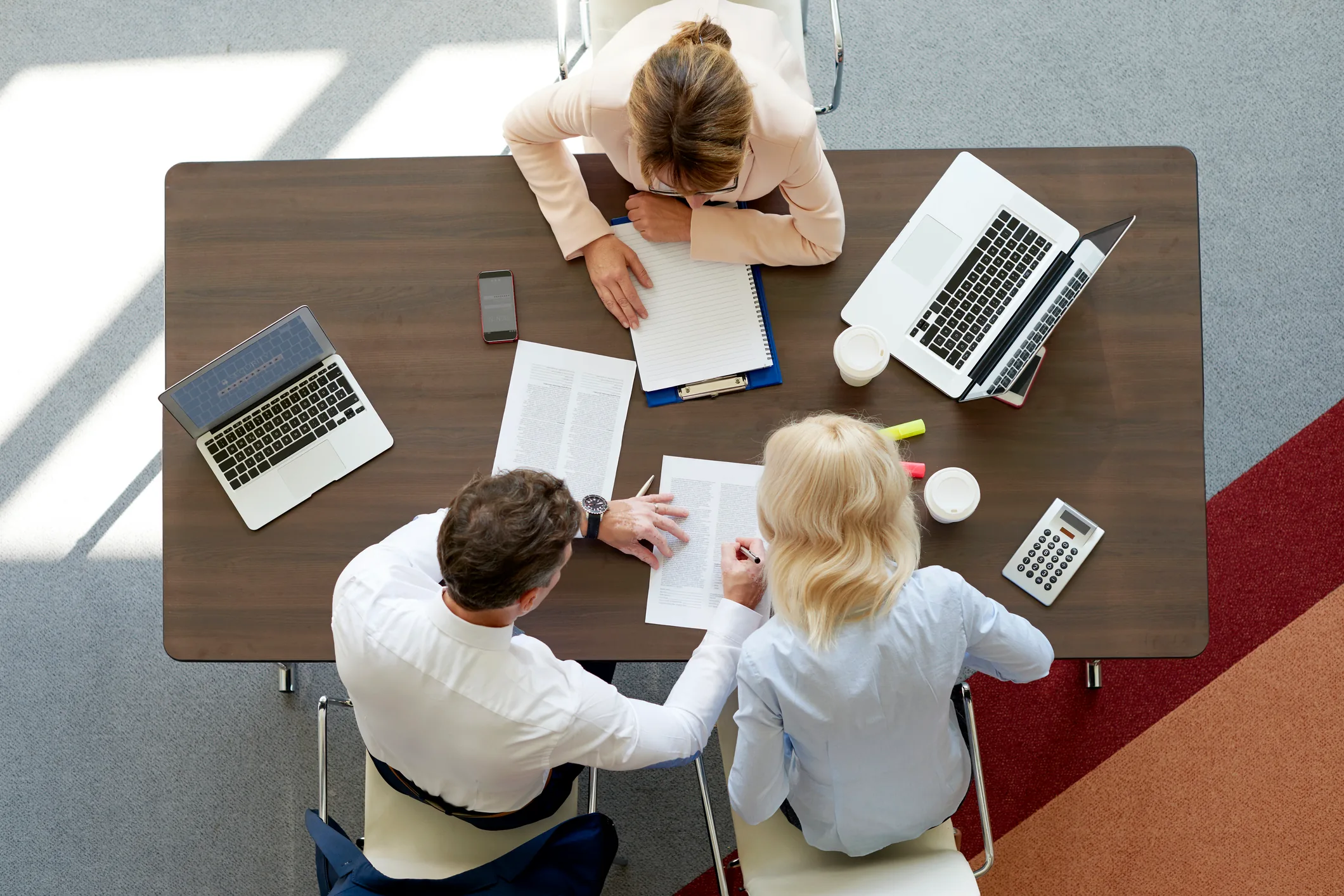 Three business professionals reviewing financial documents at a wooden table with laptops and calculator.
