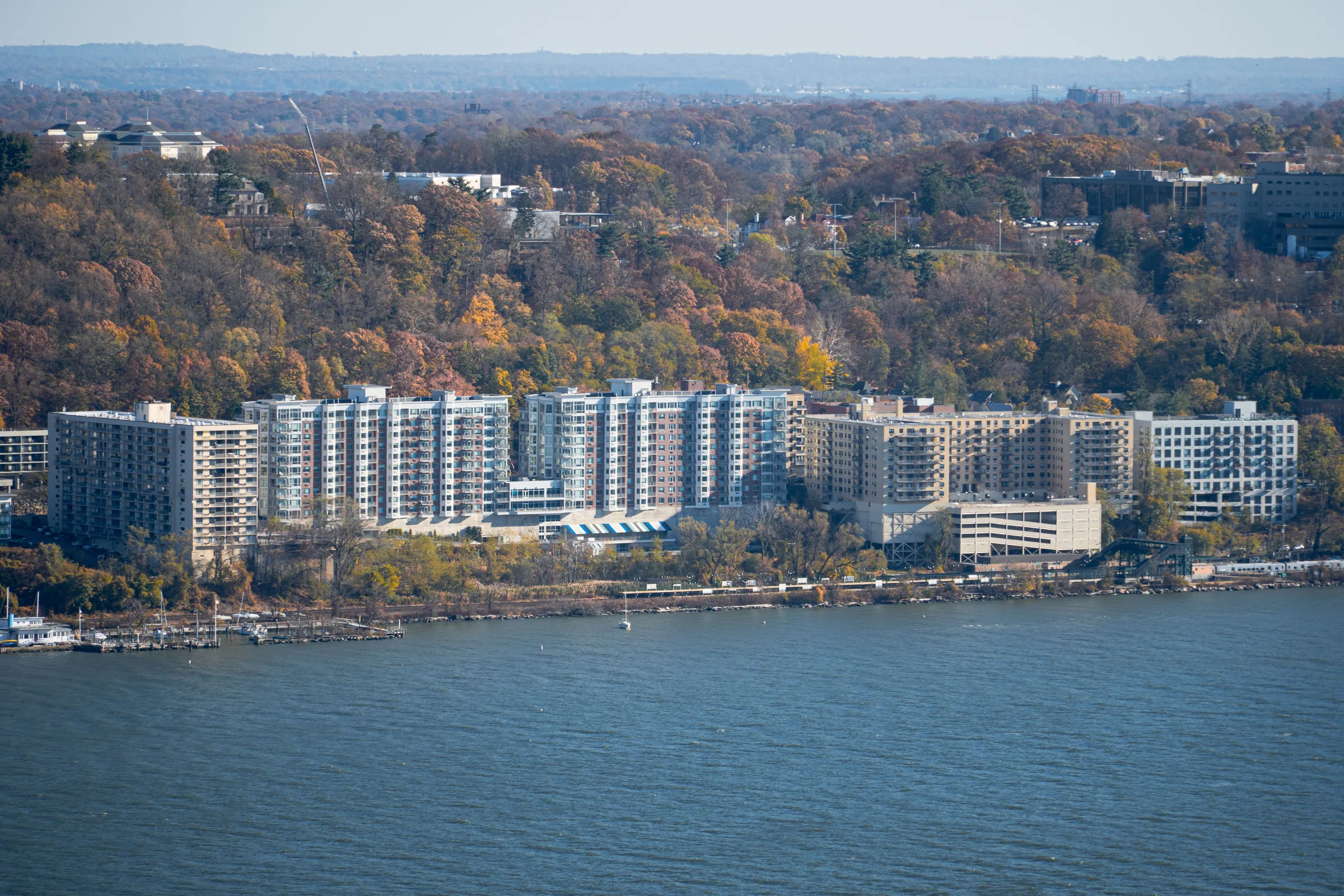 Waterfront apartment buildings and residential complex along a blue river with autumn trees in background.